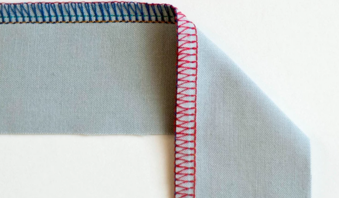 Close-up of a serger machine stitching a clean overlock edge seam on fabric