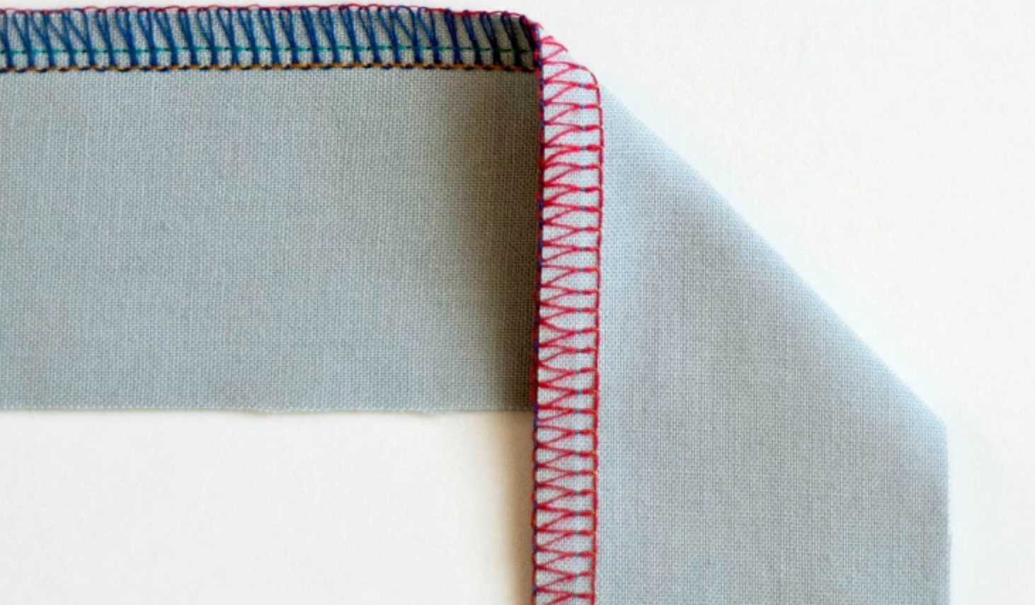 Close-up of a serger machine stitching a clean overlock edge seam on fabric